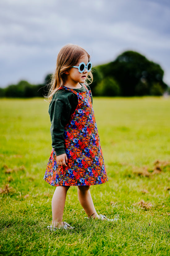 Girls handmade pinafore dress in autumn/winter floral orange and blue print. Pocket to front and button fastening straps. Available in ages 1-2 years up to 11-12 years