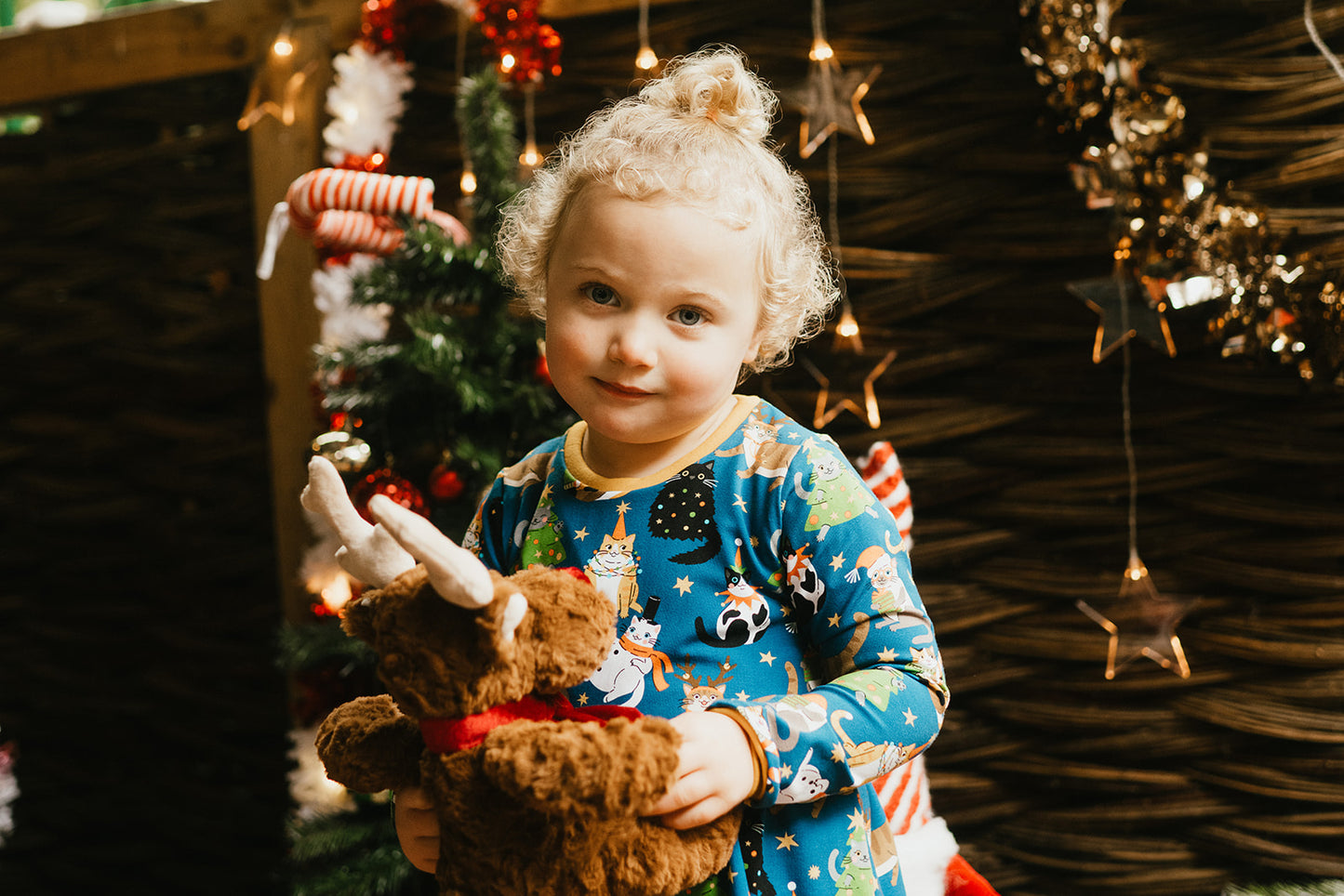 Child in festive christmas cats dress holding a teddy bear with Christmas decorations in the background