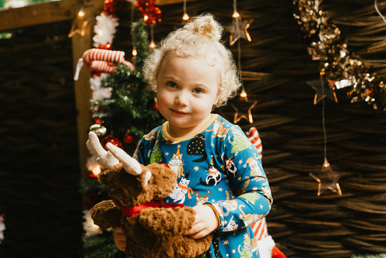 Child in festive christmas cats dress holding a teddy bear with Christmas decorations in the background
