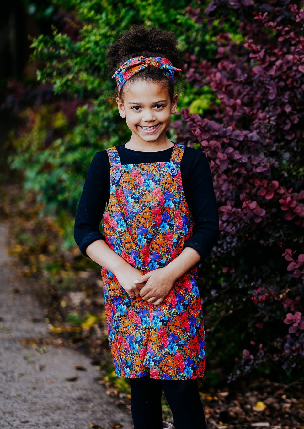 Girls handmade pinafore dress in autumn/winter floral orange and blue print. Pocket to front and button fastening straps. Available in ages 1-2 years up to 11-12 years